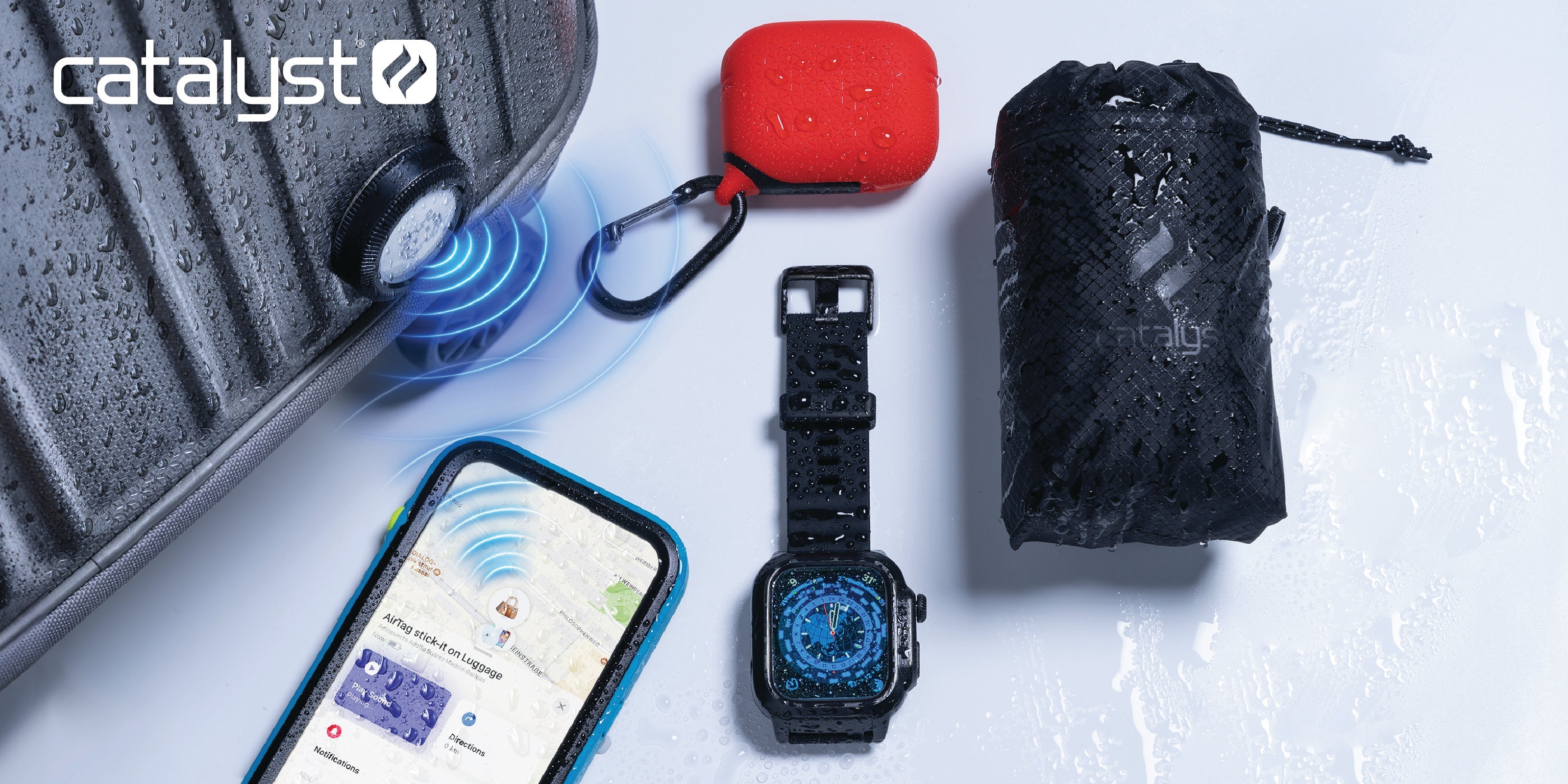 Catalyst essential travel gear featuring a black waterproof AirTag Stick-It case on a grey suitcase, a blue waterproof iPhone case, a black waterproof Apple Watch case, a red waterproof AirPods case, and a compact black waterproof backpack in its pouch.